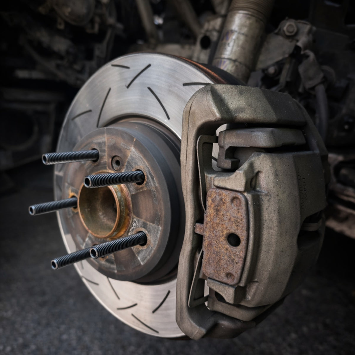 Five wheel studs installed on a BMW hub beside a slotted brake disc and caliper